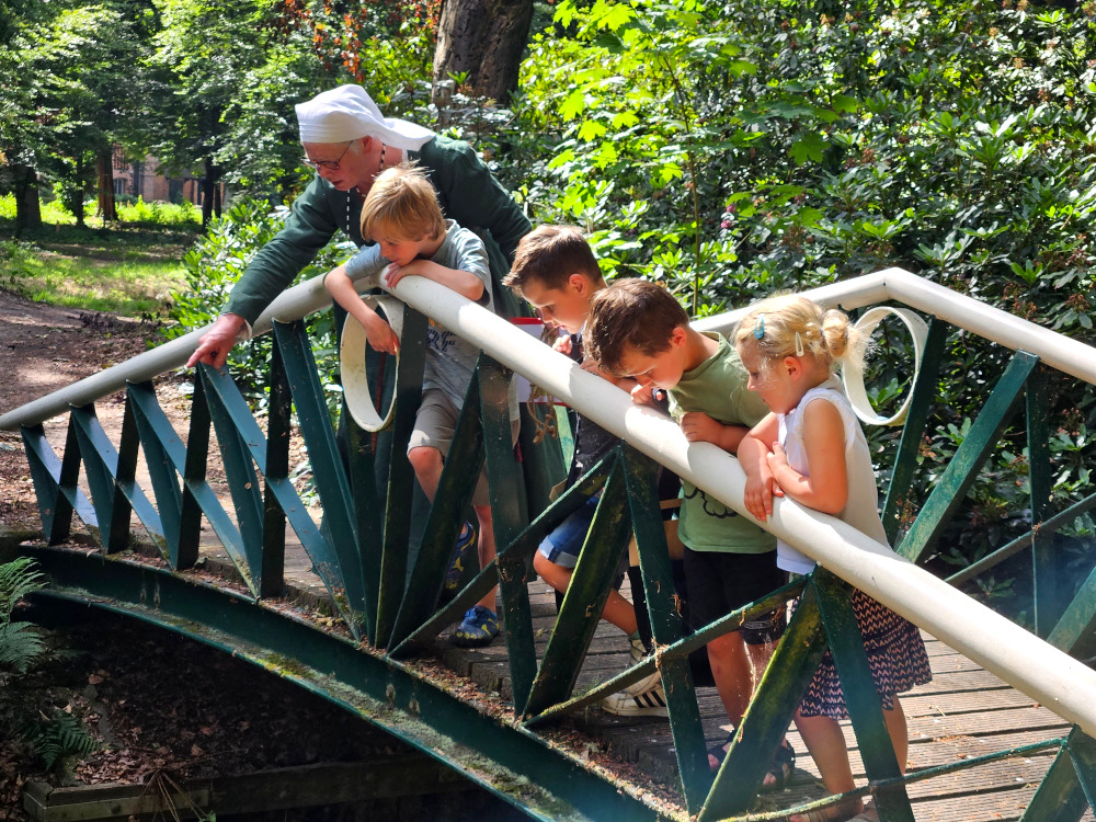 Een KidsGids staat met een groepje kinderen op een brug in het Kloosterbos.