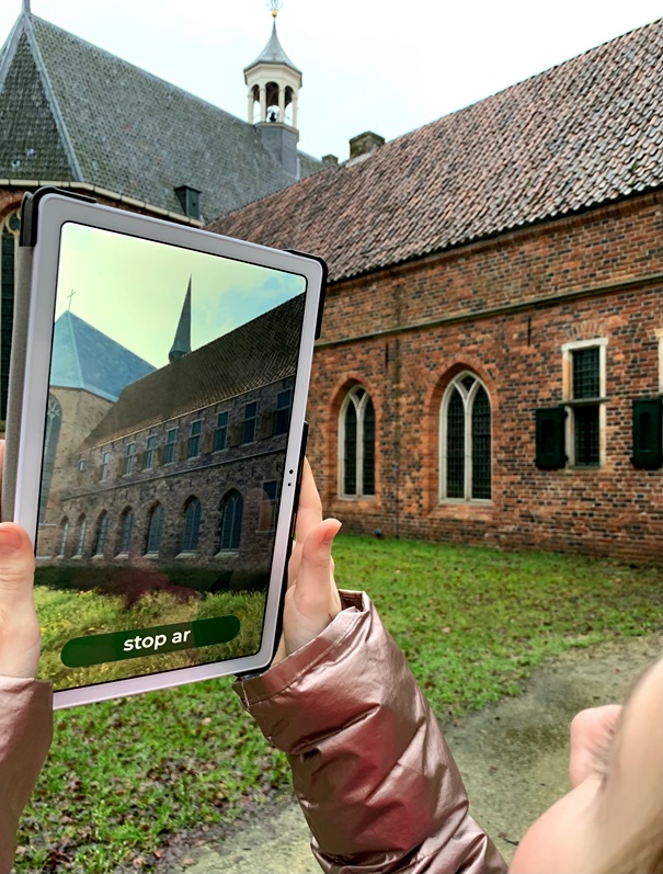 Iemand bekijkt met een tablet hoe het Klooster er eeuwen geleden uitgezien heeft.