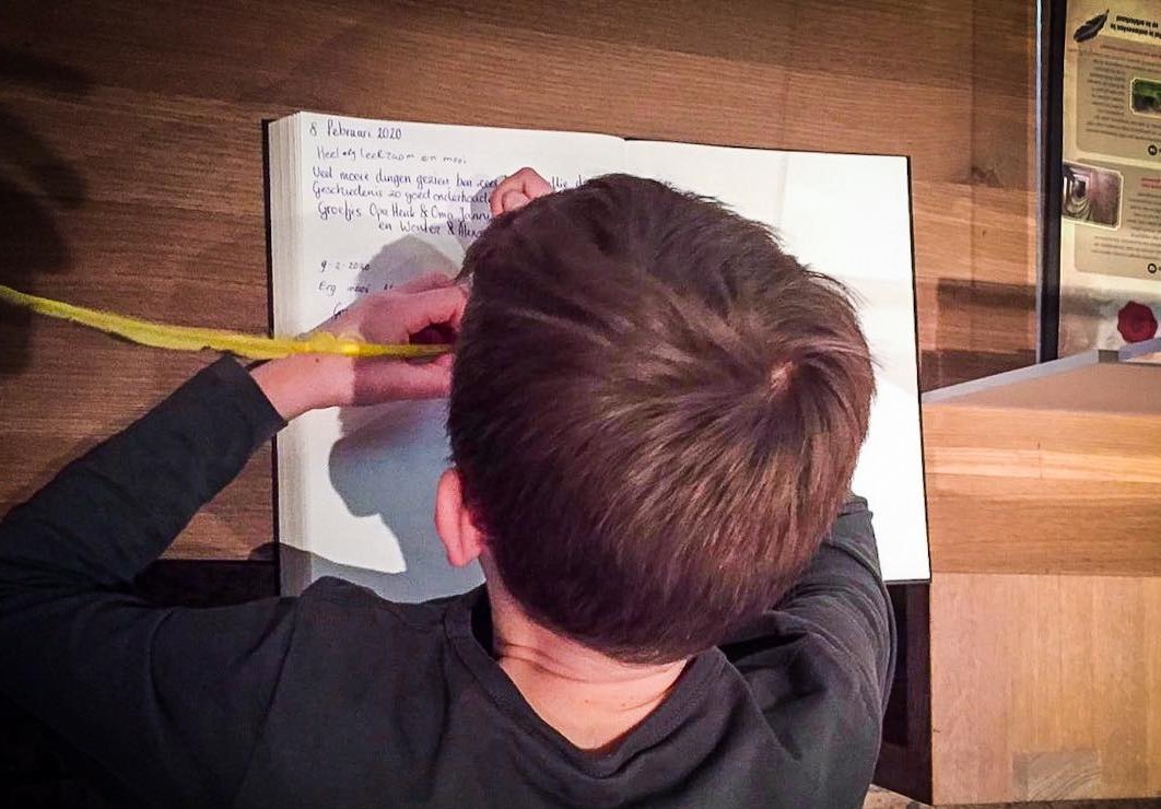 Een jongen schrijft met een ganzenveer.