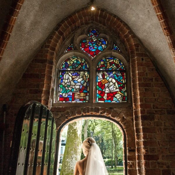 Een bruid staat in de entreedeur met veelkleurig glas-in-lood erboven.