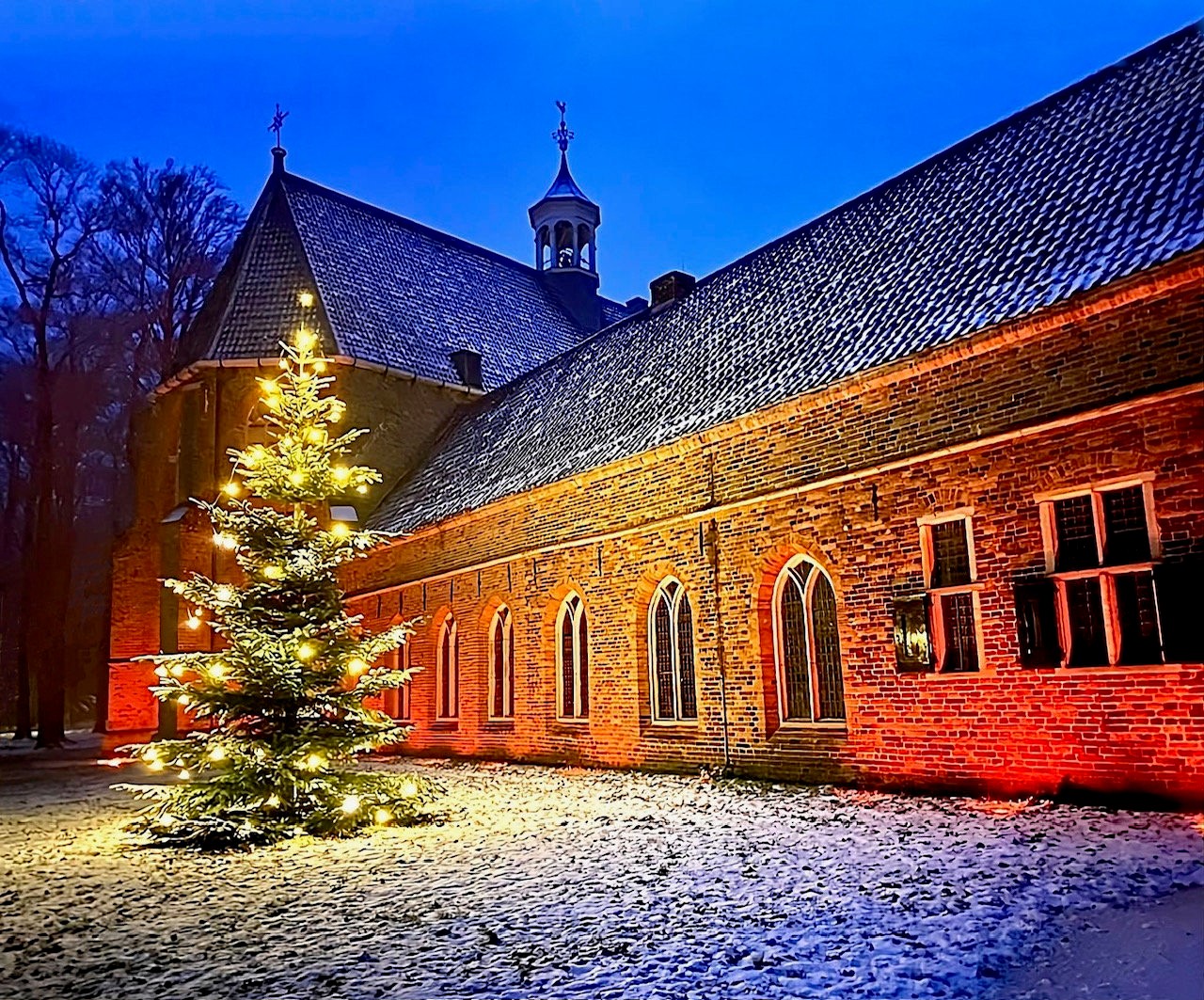 Voor het klooster staat een kerstboom in de sneeuw, met de kerktoren op de achtergrond.